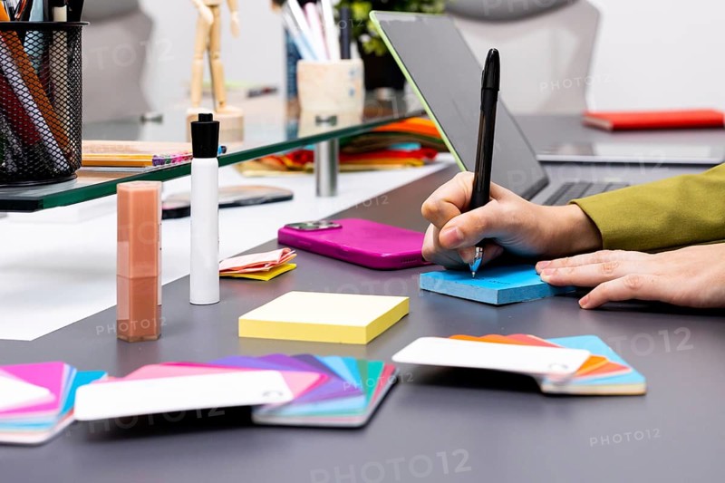 A creative workspace featuring hands writing on a blue notepad surrounded by colorful tools, showcasing a dynamic image consulting environment that sparks inspiration