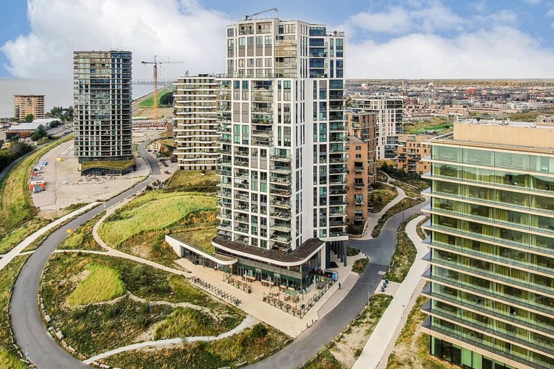 A scenic view of a contemporary apartment building surrounded by greenery and a bustling city skyline in the background. Ideal for urban architecture enthusiasts