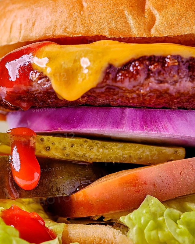 A stacked cheeseburger featuring a beef patty, melted cheese, pickles, tomato, lettuce, red onion and ketchup creating a mouthwatering layered sandwich close-up
