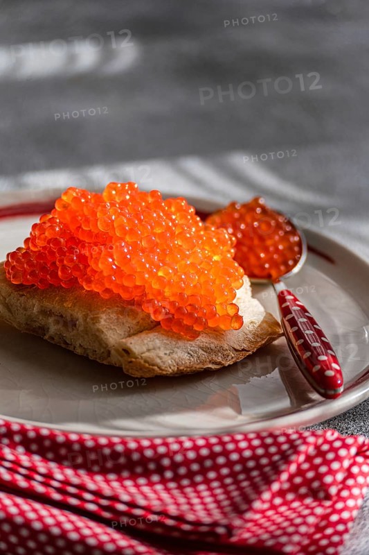 From a close-up angle, this image showcases healthy organic red caviar from trout fish, piled generously atop a slice of crusty bread. The serving dish is accented by a decorative red and white polka-dot napkin, creating a visually appealing setting ideal for food presentations and culinary themes