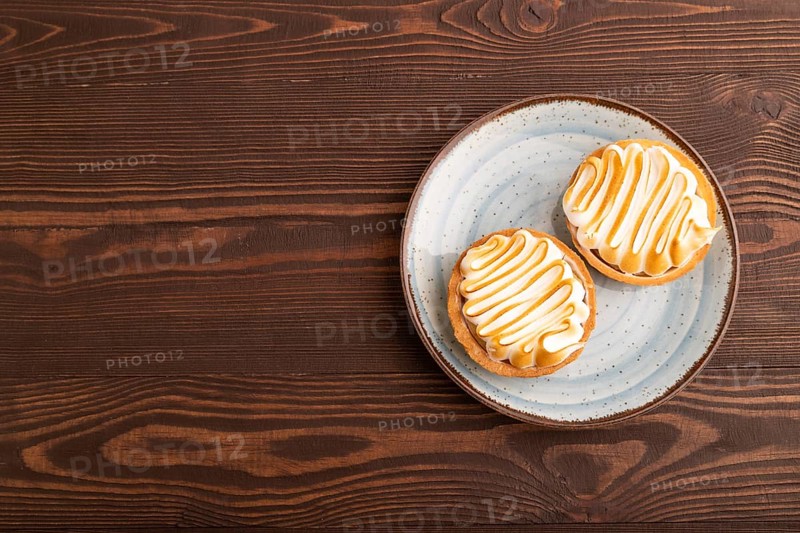 French lemon tart with meringue on brown wooden background, top view, flat lay, copy space