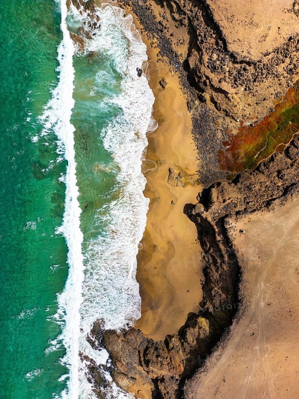 From above, this image captures a remarkable natural pool at Tindaya Beach in Fuerteventura, Canary Islands, showcasing the unspoiled beauty and contrast between the rugged shorelines and serene waters