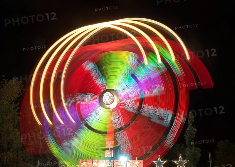 A dazzling long exposure photograph capturing the swirling motion of colorful lights on an amusement park ride against a dark sky