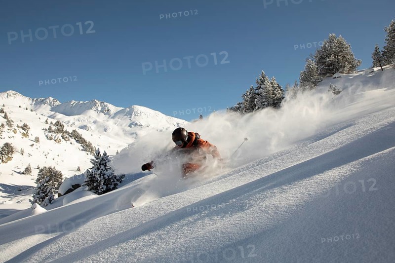 A thrilling freeride skier glides through fresh powder on a snowy mountain slope The bright blue sky provides a stunning backdrop, highlighting the dynamic motion and freedom of the sport