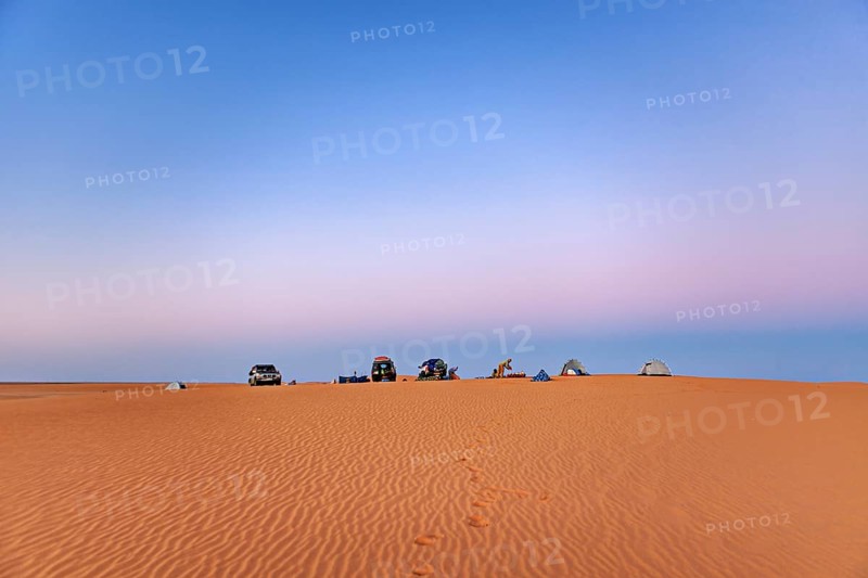 Vehicles and tents standing on a sand dune under an open sky at sunrise, camping in the sand dunes of the Sahara in Algeria
