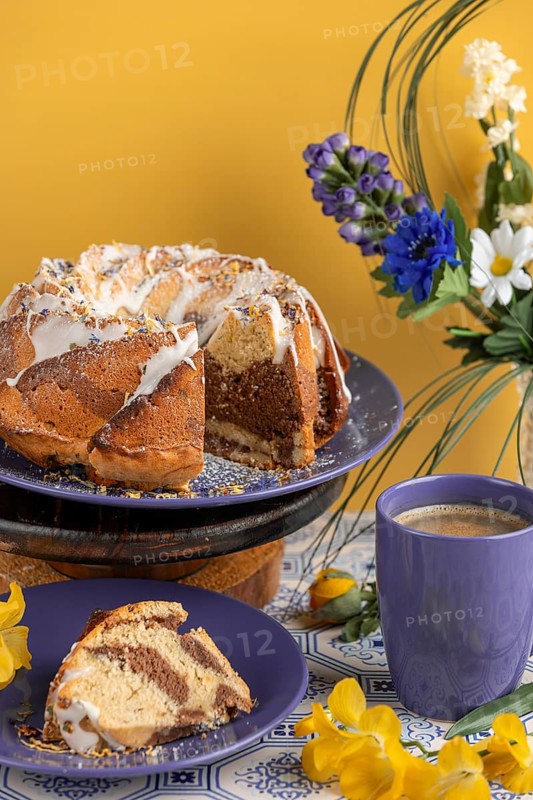 Cut marble bundt cake, cake on blue plates with icing, surrounded by flowers and a cup of coffee, yellow background