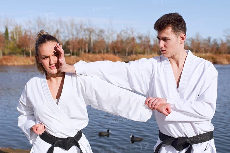 Karate experts practice combat techniques near a peaceful lake. Dressed in traditional karategi, a man and a woman focus on perfecting their martial arts skills outdoors