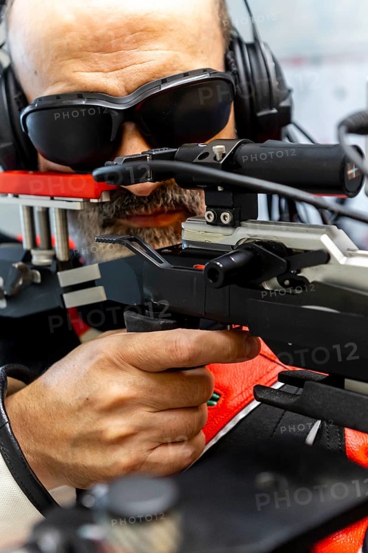 An experienced blind Olympic shooter aims with precision using advanced equipment. Wearing headphones and protective eyewear, they exemplify skill and dedication under challenging conditions