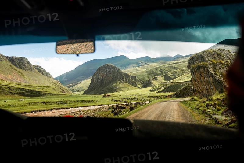 Captivating view from inside a car showing a road winding through vivid green valleys and rugged mountains in the Peruvian Andes, under a bright blue sky