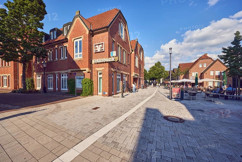 Pedestrian zone, commercial building, residential building, brick building, lantern, Volksbank Westmünsterland eG, outdoor area of a restaurant, street made of concrete paving stones and paving slabs, trees, pedestrians as a secondary motif, blue sky, cumulus clouds, Wilhelmstraße, Hermannstraße and market intersection, Lüdinghausen, Münsterland, Coesfeld district, North Rhine-Westphalia, Germany