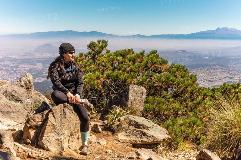 A woman sits on a rock, soaking in the stunning mountain landscape under a clear blue sky Perfect moment capturing nature's tranquility and the spirit of adventure