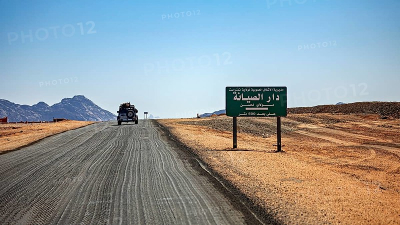 An off-road vehicle on a sandy road next to a sign in a vast desert environment, By car through the Sahara in Algeria