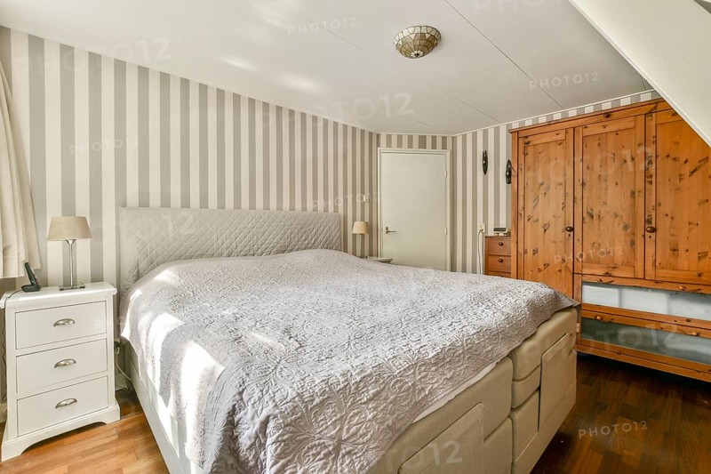A stylish bedroom showcasing a contemporary design with striped walls, wooden furniture, and soft bedding, creating a warm and inviting atmosphere