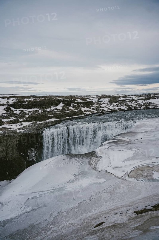Captivating view of Dettifoss waterfall in Iceland, partially frozen and surrounded by a snow-covered landscape. The power and beauty of nature are on full display