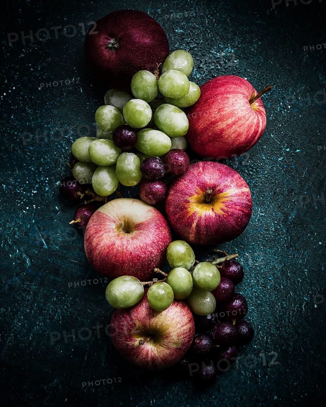 A vibrant arrangement of fresh apples and grapes on a dark, textured background. The mix of red, green, and purple hues creates an inviting and colorful display of fruits