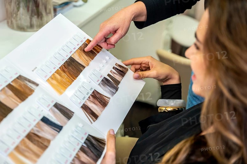 Hairdresser pointing to color options on a swatch book, assisting a client with decision making for a new hair dye style during a beauty consultation at salon