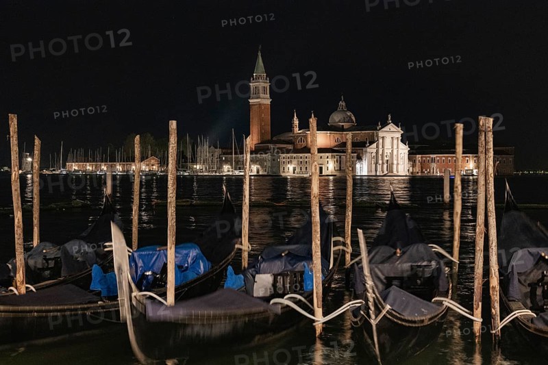 Nighttime view of San Giorgio Maggiore in Venice, Italy, showcasing the beauty of its historical architecture. The scene includes gondolas and softly lit buildings