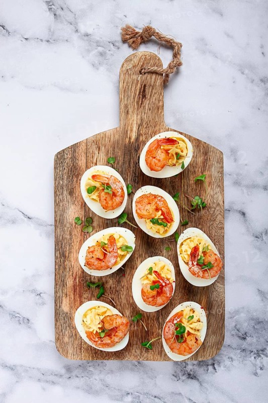 Boiled eggs stuffed with yolk and seasoned with mayonnaise, stuffed eggs with shrimp, on a wooden chopping board, selective focus, close-up, no people