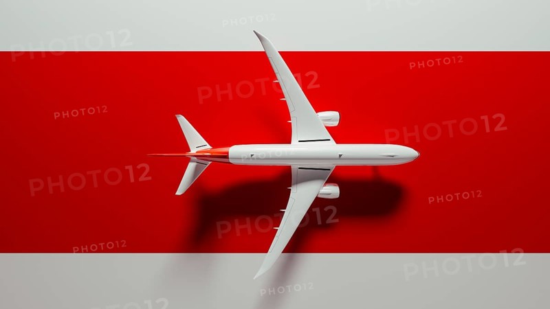 A striking commercial airplane flies over a bold red surface, symbolizing travel and adventure. Perfect representation of aviation excitement