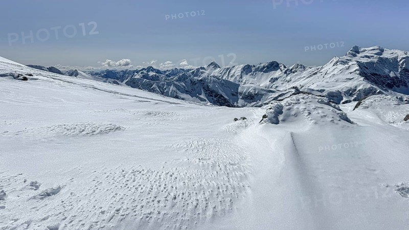 A stunning view of snow blanketed mountains under a clear blue sky, offering a serene winter landscape with untouched snow and majestic peaks in the background