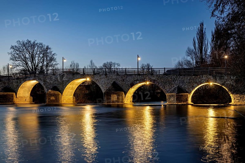 Illuminated stone bridge at night with lights reflecting in the quiet river, The Burgau Bridge in the Saale Valley near Jena in Thuringia