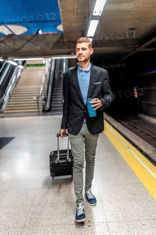 Businessman walking through a bustling subway station, carrying luggage and sipping coffee, embodies the essence of urban commuting
