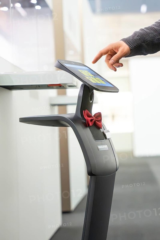 A robot-like device with a red ribbon is touched by a hand on the screen, interactive guided tours by robotic personalities from Robolutions, Pforzheim, Germany