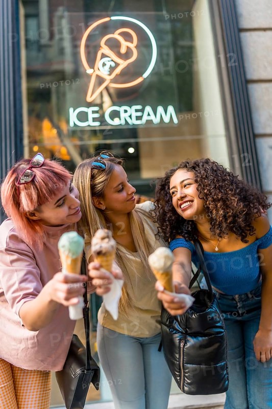 Vertical photo of three female friends showing at camera delicious ice cream cones outdoors