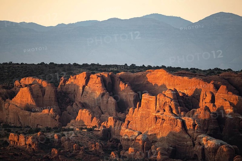 Stunning sunrise view over sandstone formations in Arches National Park, showcasing the unique geological features illuminated by the morning light against a backdrop of serene mountains