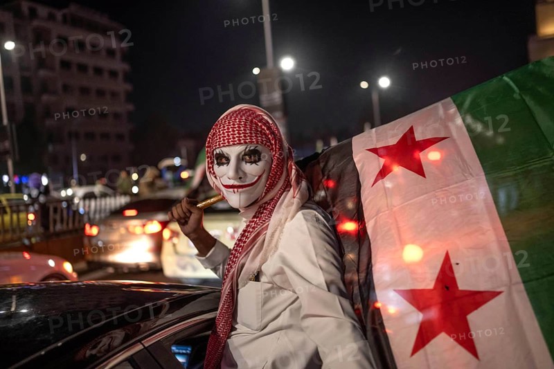 Damascus, Syria. December 7th 2025. A mask wearing Syrian and the revolutionary flag on the streets of Damascus celebrating one year since the fall of the Assad regime, Damascus Syria