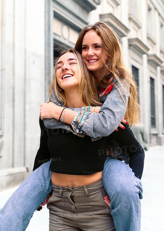 Two young women share a joyful moment in a lively city street. Their happiness and connection are evident, set against an urban backdrop