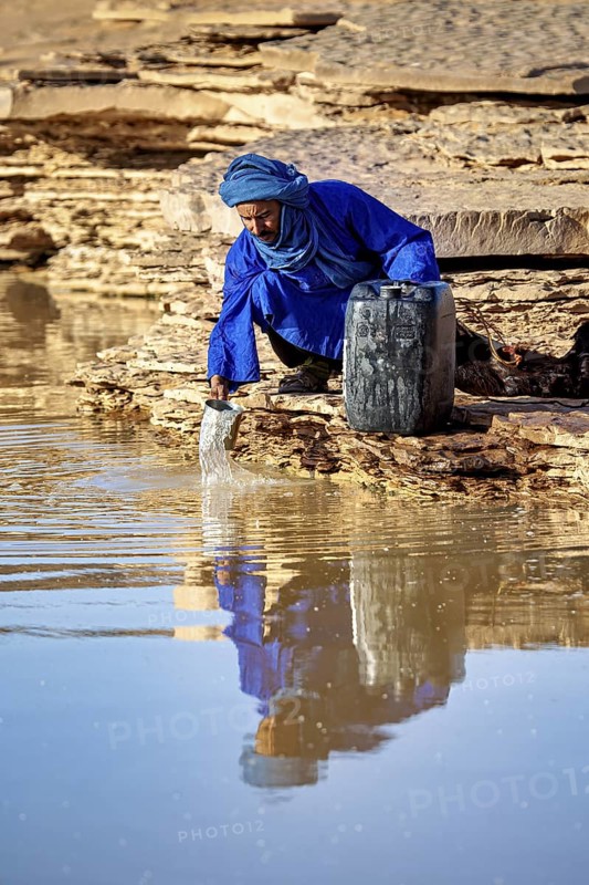 Person filling water into a canister on a rock in a dry environment, Tuareg fetching water in the Sahara in Algeria