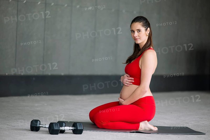 A pregnant woman in a yoga outfit practices mindful meditation on a yoga mat, focusing on wellbeing and balance. She embraces a healthy lifestyle during her pregnancy journey