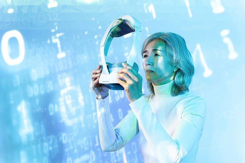 An elderly Asian woman immerses herself in the metaverse using a VR headset. The digital background symbolizes technology and futuristic exploration, reflecting modern aging