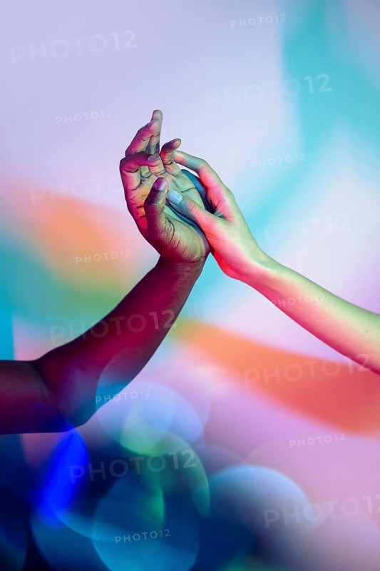 Close-up of multiethnic hands intertwined under a colorful, vibrant light, symbolizing unity and diversity. The background features soft, blurred bokeh circles, enhancing the visual harmony
