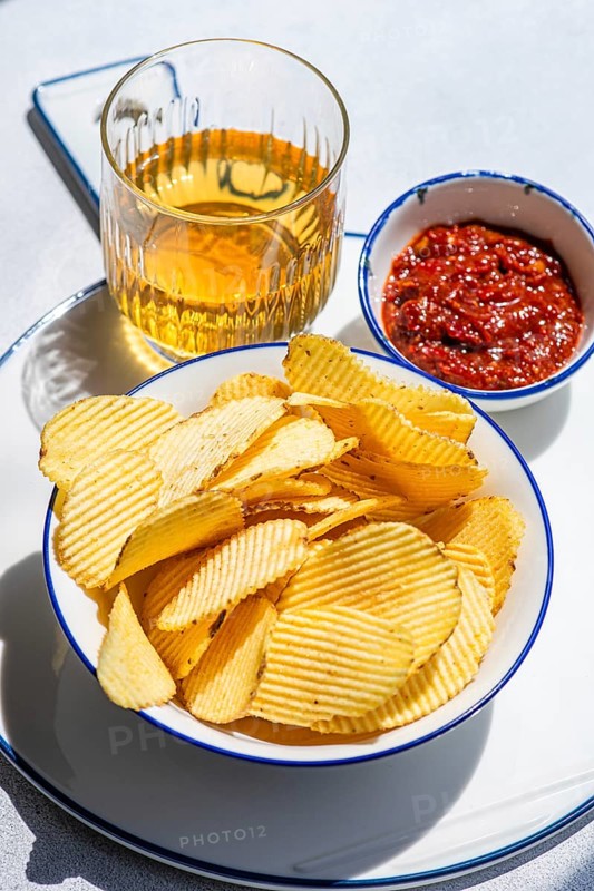 A bowl of crispy homemade chips pairs perfectly with a refreshing drink and a zesty dip. This delightful snack combination is perfect for casual gatherings or solo indulgence