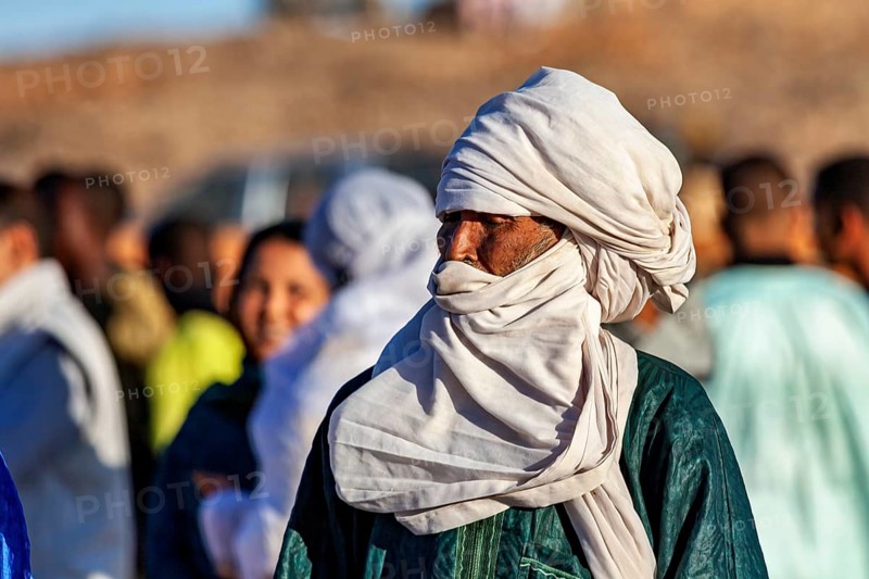 Man with turban looks to the side, surrounded by people, The traditional Tuareg at the Tamanrasset Festival in the Sahara in Algeria