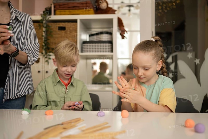 Children participate in a creative class, playing with colorful modeling clay under adult supervision. The classroom is bright and encourages imaginative expression