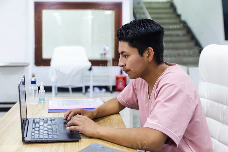 A professional in a physiotherapy clinic in Ecuador works diligently on a laptop. The modern, clean setting reflects expertise and care in a medical environment