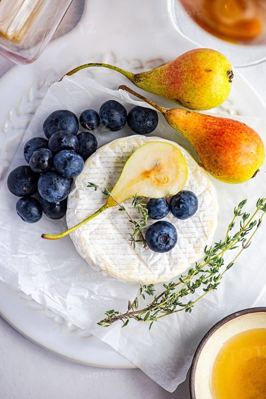 A delicious arrangement featuring gourmet brie cheese paired with ripe pears, fresh blueberries, and a sprig of thyme. This elegant setup invites indulgence and fine dining