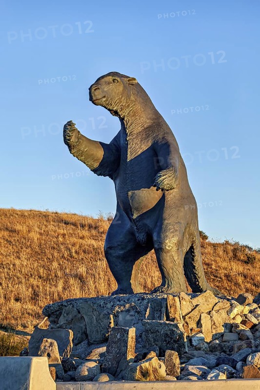 Sloth statue on rocks with hilly landscape and blue sky in the background, The statue of the giant sloth near Puerto Natales in Patagonia Chile