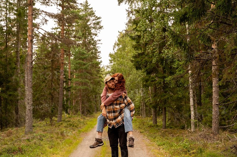 A couple shares a loving moment during a walk in a lush Swedish forest. The serene setting and vibrant greenery capture the essence of nature and romance