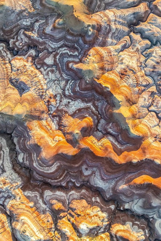 Aerial view of vibrant bentonite formations in Utah, showcasing swirling patterns and rich golden hues. These natural structures create a mesmerizing abstract landscape