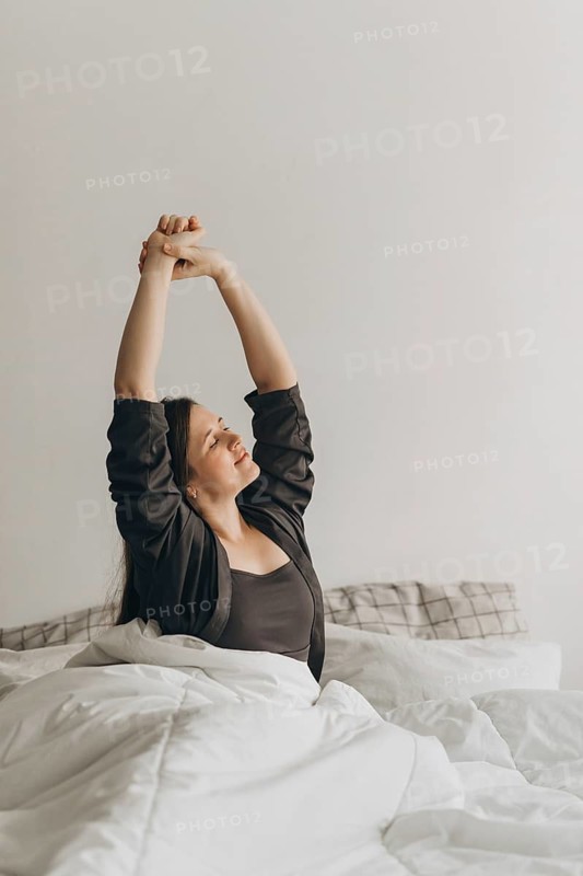 Woman stretching in bed, embracing a fresh start to her day. The image symbolizes a healthy morning routine, essential for wellness and energy, often recommended by nutritionists