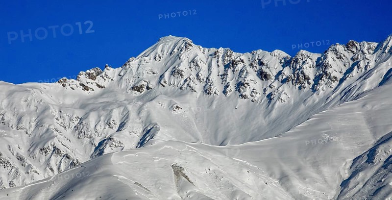 Snow-capped mountain peaks rise majestically against a clear blue sky, showcasing a serene winter landscape in Georgia The crisp white snow contrasts with the deep blue, creating a breathtaking view