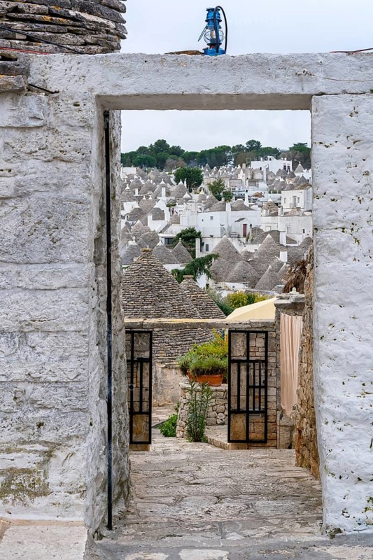 Picturesque view of Alberobello's iconic Trullo rooftops framed by a stone archway, highlighting the charming architecture and heritage of Puglia, Italy