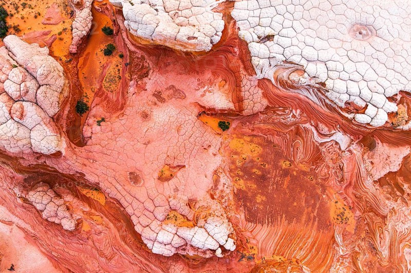 Aerial shot capturing the striking abstract patterns of red and white rocks. The textures and colors blend naturally, creating a vivid, artistic landscape