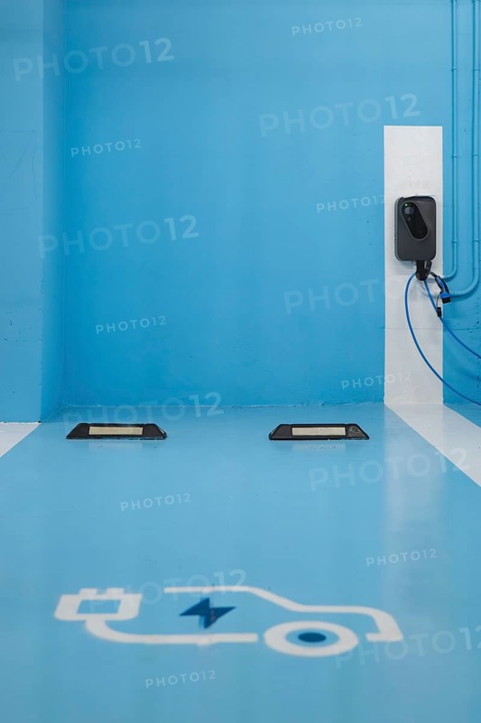 A electric car charging station, featuring a charger mounted on a blue wall and designated blue parking spots marked with white electric car symbols