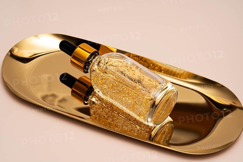 A premium anti-aging face serum infused with golden particles, elegantly presented on a reflective gold tray, emphasizing luxury skincare