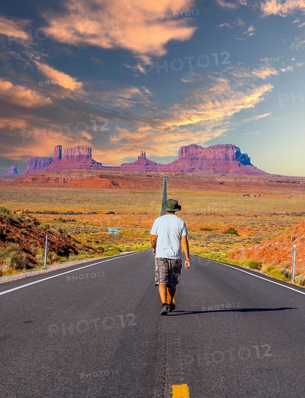 A young man in a white shirt walking on the road to Monument Valley in sunset. Utah